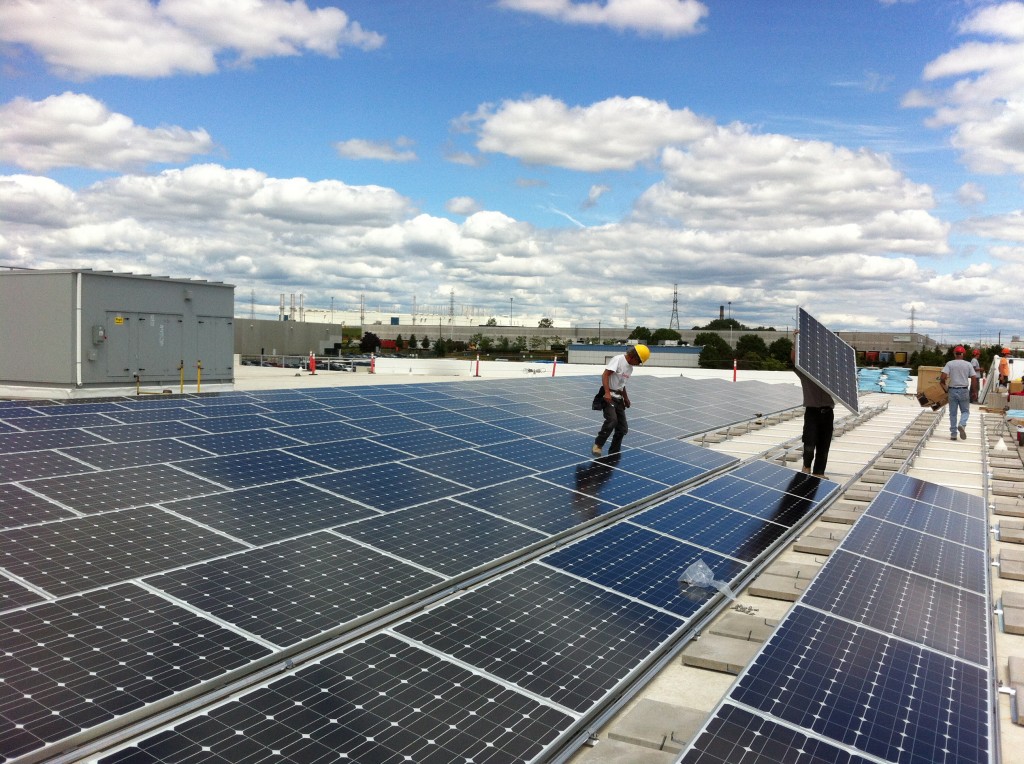 Professional workers installing solar panels on the roof of a large industrial warehouse under a clear blue sky.