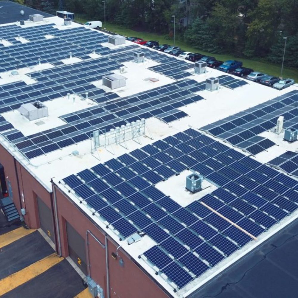 Solar panels visibly installed on the roof of a brown industrial warehouse, symbolizing renewable energy usage.